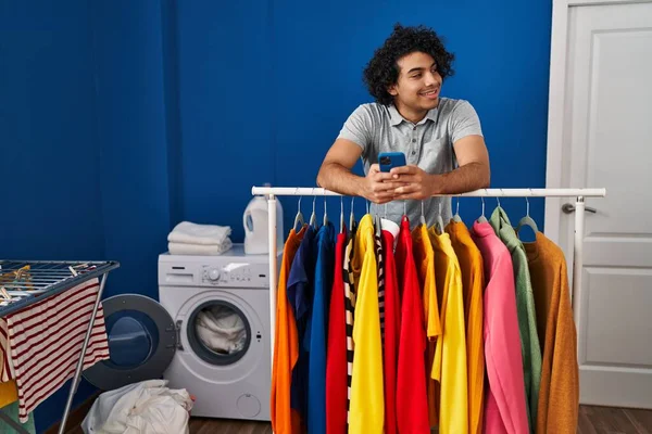 在洗衣房用智能手机靠在架子上的年轻人 — 图库照片