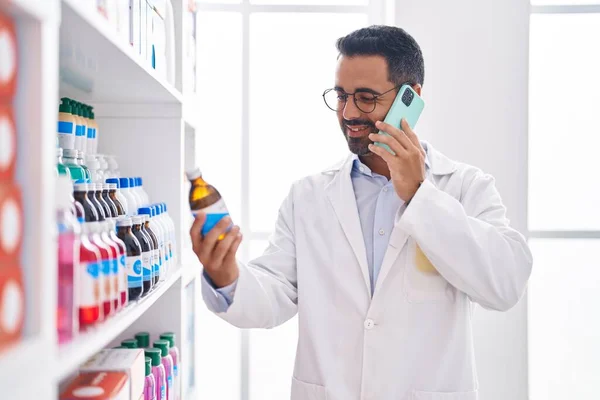 Jovem Hispânico Homem Farmacêutico Segurando Garrafa Medicação Falando Smartphone Farmácia — Fotografia de Stock