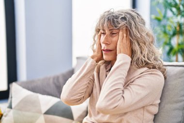 Orta yaşlı bir kadın evdeki kanepede otururken baş ağrısı çekiyor.