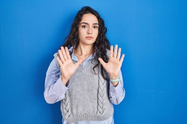 Mavi arka planda duran esmer bir kadın. Avuçlarını hareket ettiriyor. Korkmuş ve iğrenç bir ifadeyle reddediyor. Dur ve yasakla. 