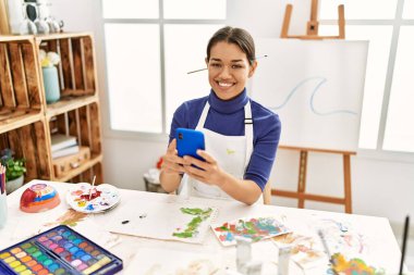 Sanat stüdyosunda akıllı telefon çizimi yapan genç Latin bir kadın.