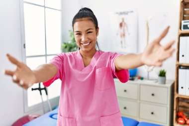 Ağrı kesici kliniğinde çalışan genç İspanyol kadın kameraya sarılıp gülümsüyor. Mutluluğu kucaklayan neşeli bir ifade.. 