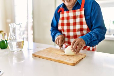Son sınıf öğrencisi gülümsüyor. Mutfakta soğan doğruyor.