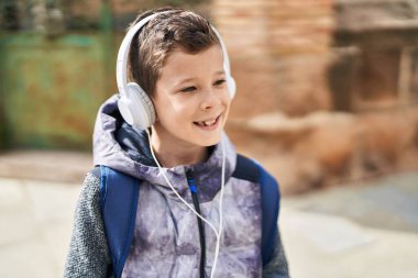 Sarışın çocuk kendinden emin bir şekilde gülümsüyor, sokakta müzik dinliyor.