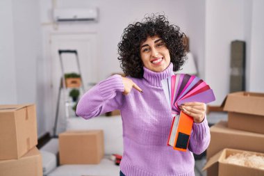 Yeni ev duvarının rengini seçen kıvırcık saçlı genç esmer kadın gülümseyen mutlu ve gururlu birini işaret ediyor. 