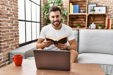 Genç İspanyol adam gülümsüyor evde kendinden emin bir şekilde kitap okuyor.