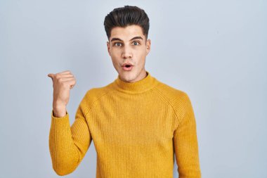 Mavi arka planda dikilen İspanyol genç adam elleri yana doğru işaret ederek şaşırdı, ağzı açık hayret içinde kaldı.. 