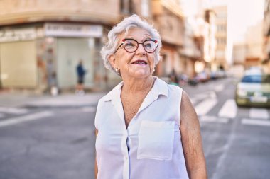 Yaşlı, kır saçlı, gülümseyen bir kadın sokakta kendine güveniyor.