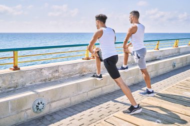 Two hispanic men couple stretching at seaside