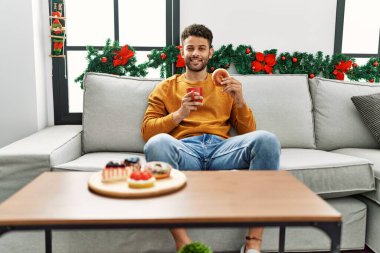 Genç bir Arap kahvaltısını yapıyor. Yılbaşı dekoru için kanepede oturuyor..