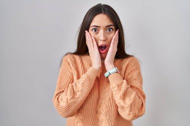 Beyaz arka plan üzerinde duran genç esmer kadın korkmuş ve şok olmuş, şaşırmış ve şaşkın bir yüz ifadesi var. 