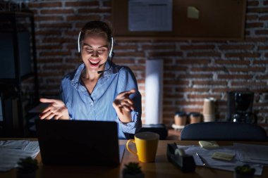 Geceleri ofiste çalışan güzel esmer kadın kucaklaşmak için kollarını açmış gülümseyen kameraya bakıyor. Mutluluğu kucaklayan neşeli bir ifade.. 
