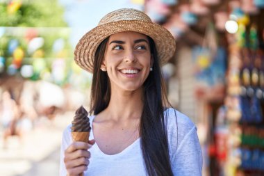 Latin kökenli genç bir turist sokak pazarında dondurma yiyerek gülümsüyor.