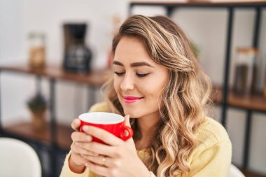 Evdeki masada kahve içen genç bir kadın.