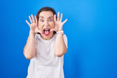 Orta yaşlı İspanyol bir kadın mavi arka planda dikiliyor. Gülümsüyor, gülümsüyor ve elleriyle bir yuhalamaya bakıyor. Şaşırdım ve çıktım. 