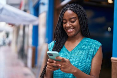 Afro-Amerikalı kadın sokakta akıllı telefon kullanarak kendine güveniyor.