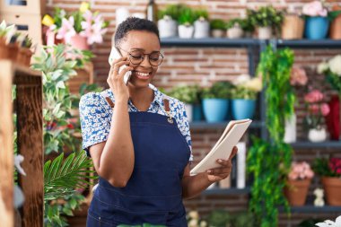 Afrikalı Amerikalı kadın çiçekçi çiçekçide akıllı telefondan not defteri okuyor.