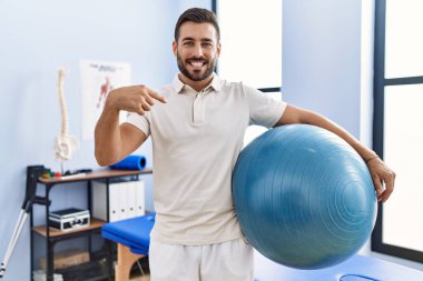 Rehabilitasyon kliniğinde elinde pilates topu tutan yakışıklı bir İspanyol mutlu ve gururlu birini işaret ediyor. 