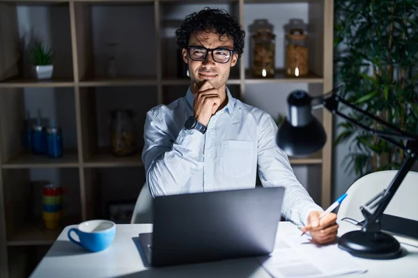 Hispanic man working at the office at night thinking worried about a question, concerned and nervous with hand on chin