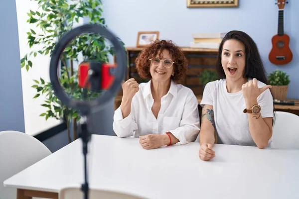 中年妇女和女儿在家里用智能手机记录Vlog教程 手指指向旁边笑着张开嘴 — 图库照片