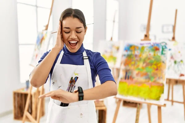 Young brunette woman at art studio looking at the watch time worried, afraid of getting late