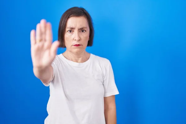 青い背景の上に立っている中年のヒスパニック系の女性は手の手のひらで歌うのを停止します 顔に負の重大なジェスチャーで — ストック写真