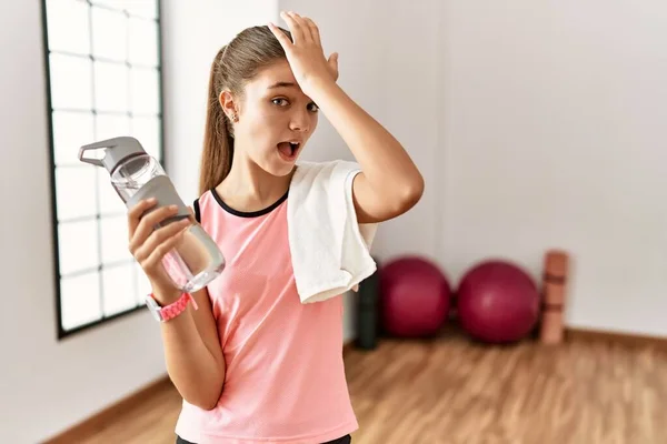 Joven Adolescente Morena Con Ropa Deportiva Sosteniendo Botella Agua Sorprendida —  Fotos de Stock