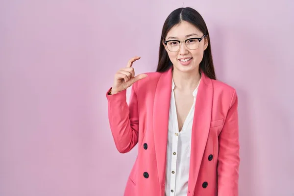 指を見てカメラで小さなサイズのサインをする手で眼鏡を笑顔と自信を持ってジェスチャーを身に着けている中国のビジネス若い女性 概念を測定し — ストック写真