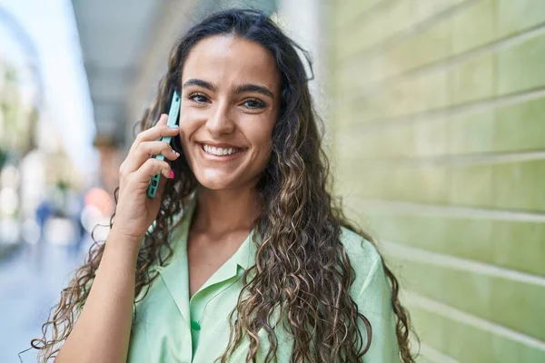 Genç, güzel, İspanyol bir kadın gülümsüyor ve caddede akıllı telefondan konuşuyor.