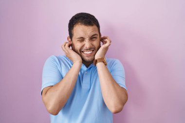 Pembe arka planda duran İspanyol bir adam yüksek sesli müzik sesi için parmaklarıyla kulaklarını kapatıyor. sağır kavramı. 