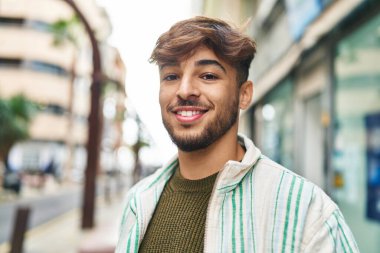 Genç Arap adam sokakta kendine güvenerek gülümsüyor.