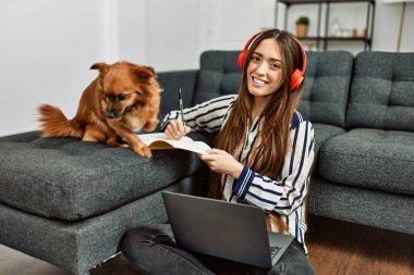 Genç İspanyol kadın dizüstü bilgisayar kullanıyor. Evde köpekle oturuyor.