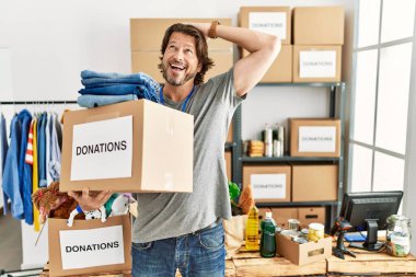 Gönüllü olarak bağış kutusunu tutan yakışıklı orta yaşlı bir adam gülümseyerek saçlarına dokunarak çekici ve modaya uygun bir poz veriyor. 