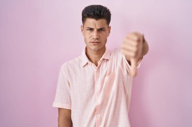 Pembe arka planda duran Latin kökenli genç adam mutsuz ve kızgın görünüyor. Reddedilmiş ve olumsuz bir hareket sergiliyor. kötü ifade. 
