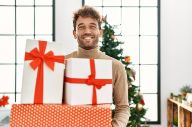 Evde kendine güvenen genç İspanyol adam Noel hediyelerini tutuyor.