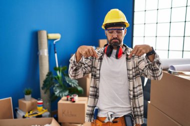 Sakallı, ev tadilatında çalışan, üzgün ve üzgün görünen, parmaklarıyla yön gösteren mutsuz ve depresif bir İspanyol.. 