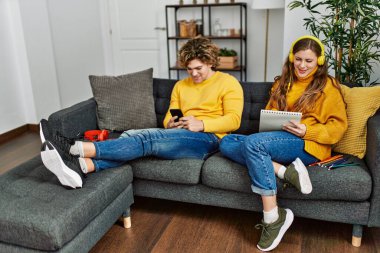 Akıllı telefon kullanan beyaz bir çift müzik dinliyor ve evde resim çiziyor.