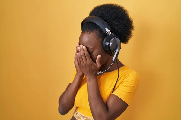 泣きながら手で顔を覆う悲しい表情のヘッドフォンを身に着けて黄色の背景に立って巻き毛を持つアフリカの女性 うつ病の概念 — ストック写真