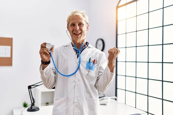 Mladý Blonďatý Muž Uniformě Lékaře Drží Stetoskop Klinice Křičí Hrdě — Stock fotografie
