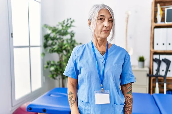 Medelålders Gråhårig Kvinna Bär Sjukgymnast Uniform Läkarmottagningen Blinkar Tittar Kameran — Stockfoto