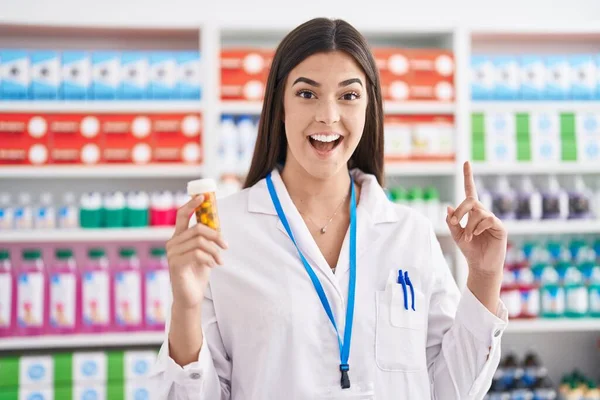 Mujer Hispana Trabajando Farmacia Sosteniendo Píldoras Sorprendida Con Una Idea — Foto de Stock