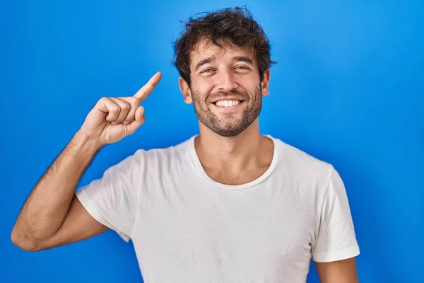 Spaanse Jongeman Die Een Blauwe Achtergrond Staat Glimlachen Wijzend Naar — Stockfoto