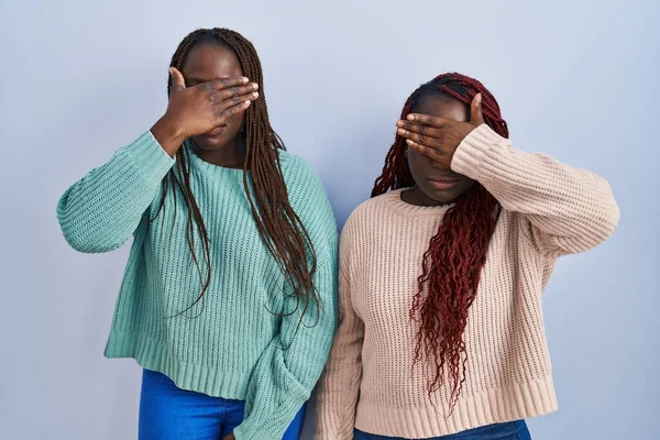 Две Африканки Стоящие Синем Фоне Закрывая Глаза Рукой Выглядят Серьезными — стоковое фото