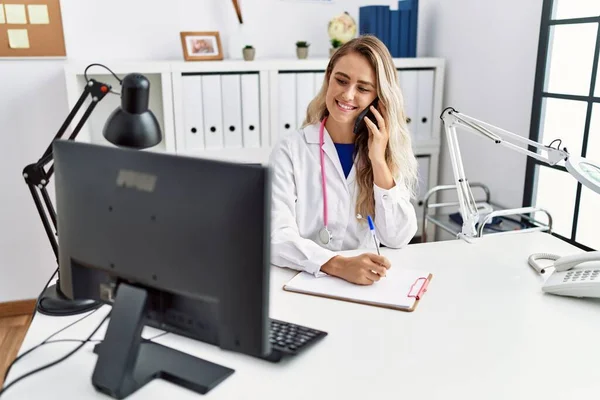 Young Woman Wearing Doctor Uniform Writing Document Talking Smartphone Clinic — Stock Photo, Image