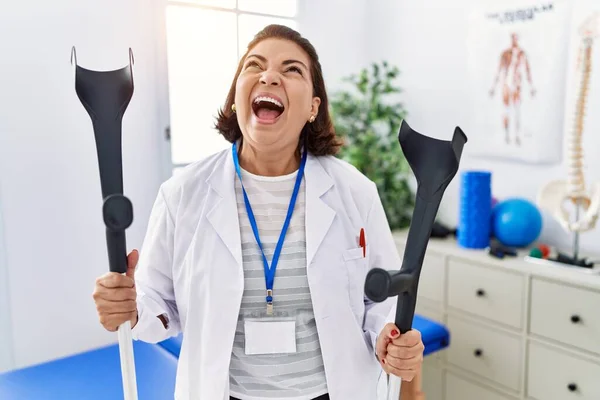 Middle Age Hispanic Physiotherapy Woman Holding Crutches Angry Mad Screaming — Stock Photo, Image