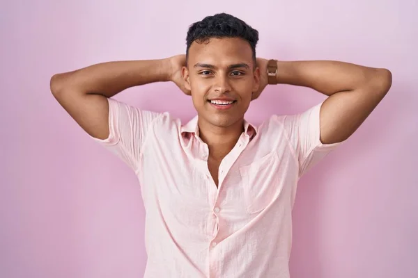 ピンクの背景の上に立っている若いヒスパニック系の男リラックスしてストレッチ 腕と手頭と首の後ろに笑顔幸せ — ストック写真