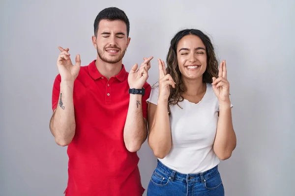 Giovane Coppia Ispanica Piedi Sfondo Isolato Gesticolando Dito Incrociato Sorridendo — Foto Stock