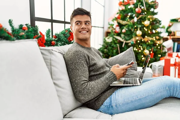 Young Hispanic Man Using Laptop Smartphone Sitting Sofa Christmas Tree — Foto de Stock