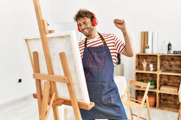 年轻的他的惊慌失措的男人带着自信的笑容在艺术工作室里画画和听音乐 — 图库照片