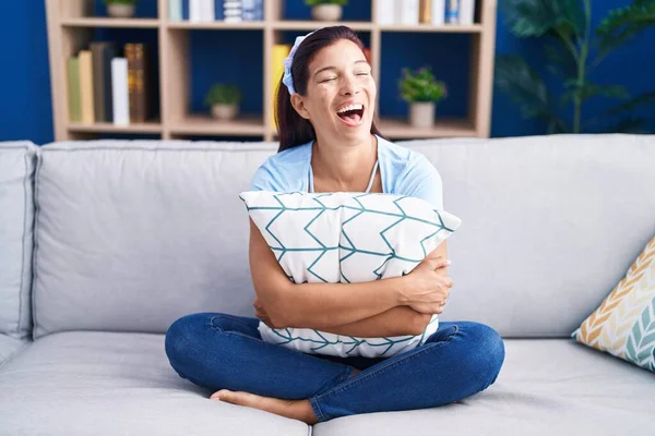Young Hispanic Woman Hugging Pillow Sitting Sofa Smiling Laughing Hard — Stock Photo, Image